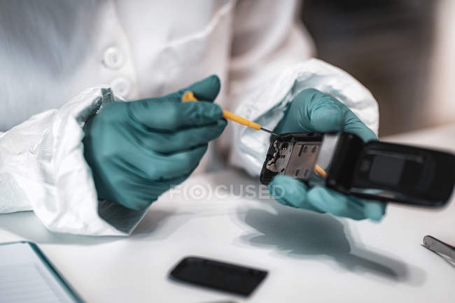 Experto forense policial examinando teléfono móvil confiscado en laboratorio científico . - foto de stock