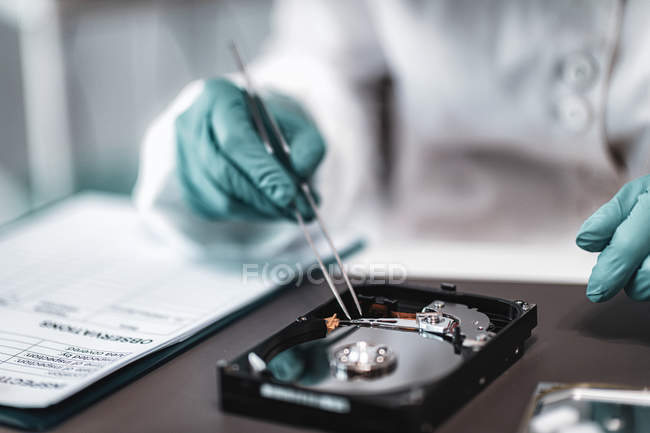 Female digital forensic expert examining computer hard drive with tweezers in police science laboratory. — Stock Photo