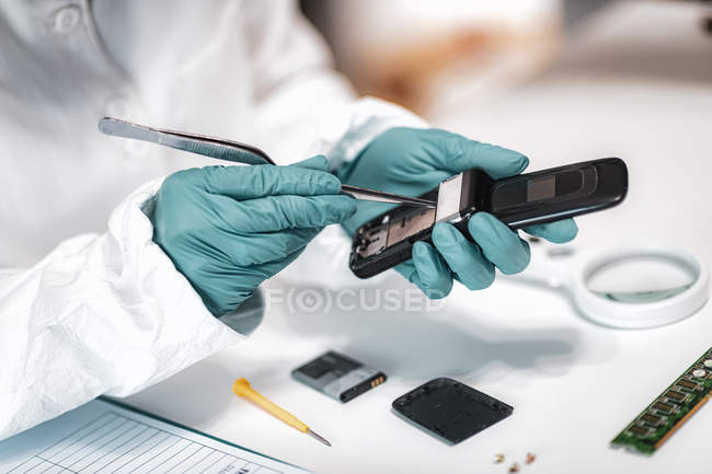Police forensic expert examining confiscated mobile phone in science laboratory. — Stock Photo