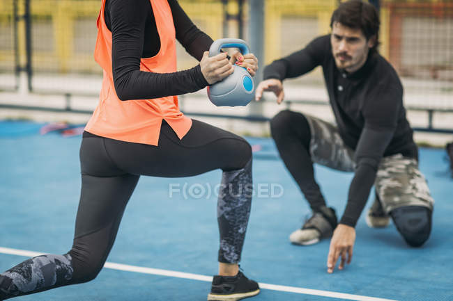 Entrenador personal de fitness que trabaja con una mujer haciendo ejercicio de pesas al aire libre . - foto de stock