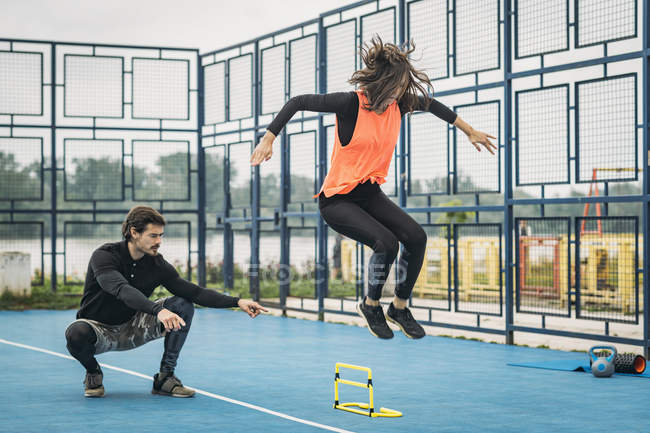 Sporty woman jumping over hurdle with fitness coach assistance. — Stock Photo