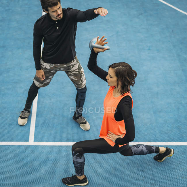 Молодая спортсменка поднимает гирь во время работы с личным тренером по фитнесу . — стоковое фото