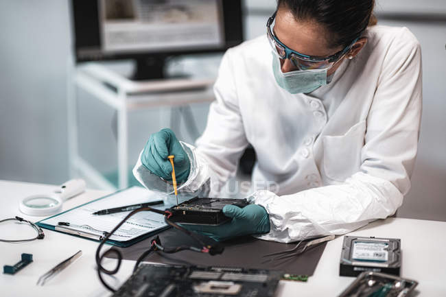 Female digital forensic expert examining computer hard drive in police science laboratory. — Stock Photo