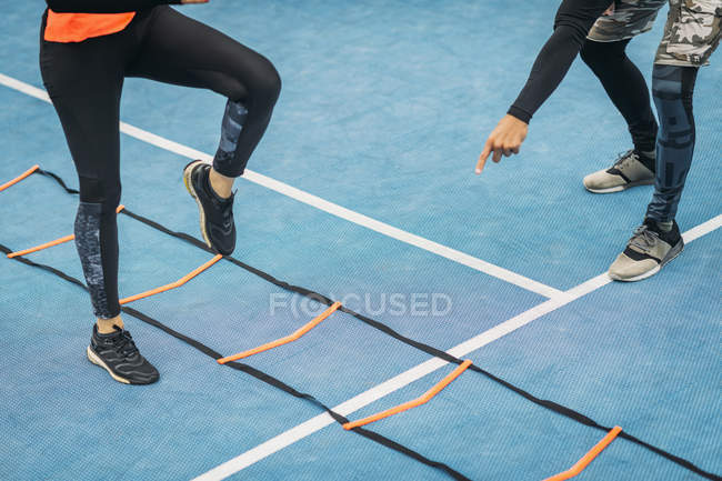 Legs of woman exercising with personal fitness coach using agility ladder. — Stock Photo