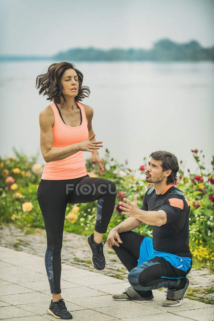 Young woman exercising running marathon by river with personal trainer. — Stock Photo