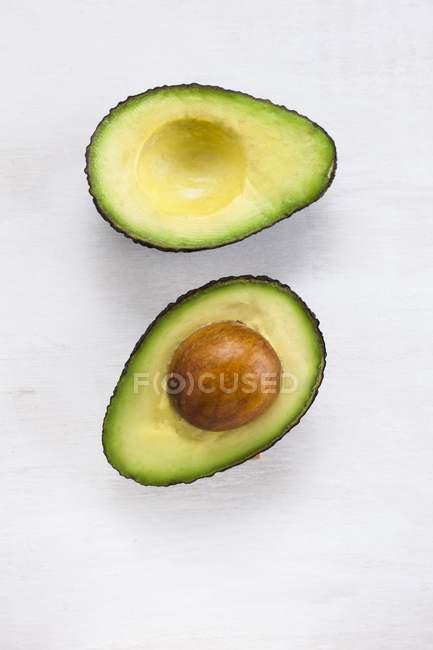 Halves of avocado with stone on white background. — Stock Photo