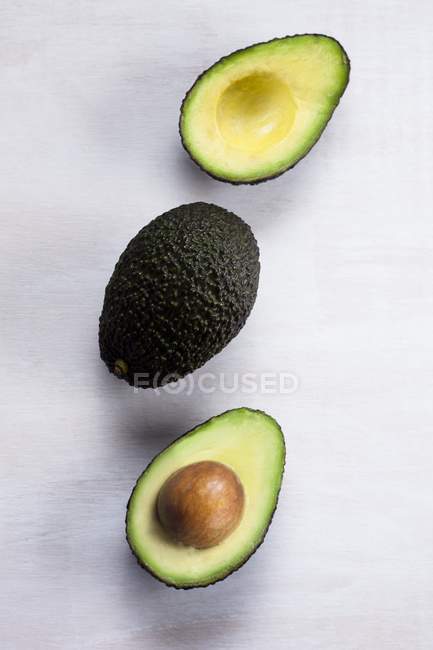Avocado whole and cut in half with stone on white background. — Stock Photo