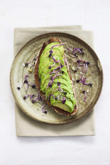 Healthy vegan snack of fresh avocado on toast with sprouts on round plate. — Stock Photo