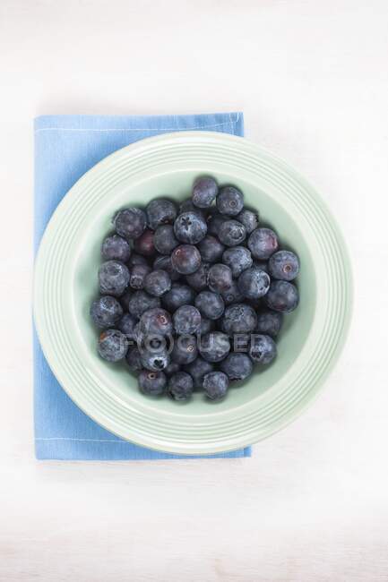 Bleuets dans une assiette sur une serviette bleue sur la table, vue sur le dessus . — Photo de stock