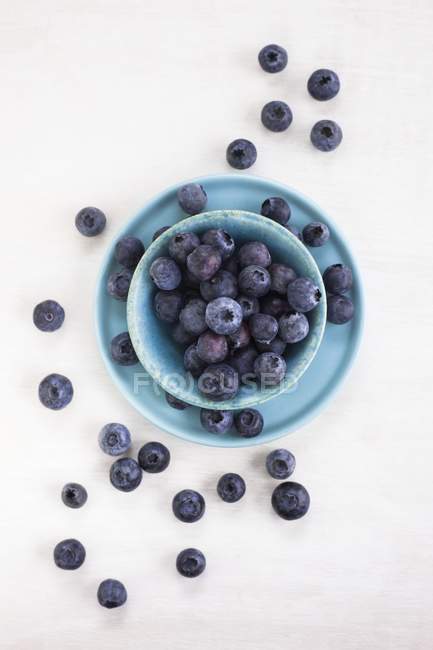 Bleuets dans un bol et assiette sur fond blanc, vue de dessus . — Photo de stock