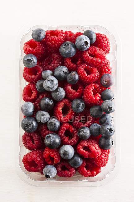 Plastic container full of raspberries and blueberries. — Stock Photo