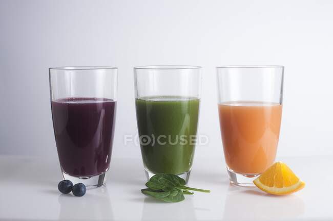 Vasos de zumos frescos hechos de bayas, naranja y hojas verdes . - foto de stock