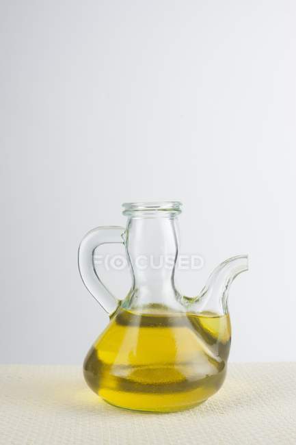 Krug mit Olivenöl auf dem Tisch auf weißem Hintergrund. — Stockfoto