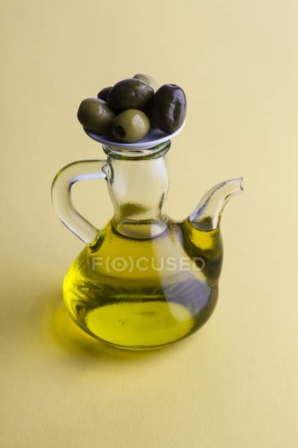 Jug of olive oil with olives on table, high angle view. — Stock Photo