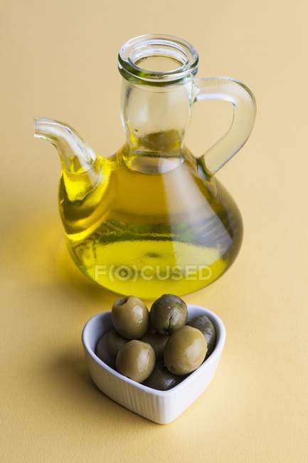 Jug of olive oil with olives in heart shaped dish. — Stock Photo