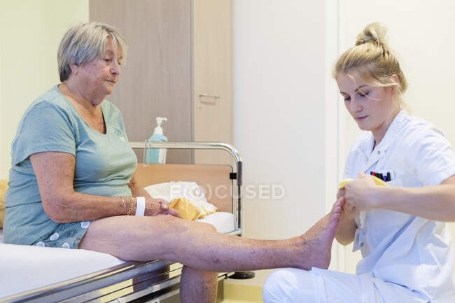 Госпиталь Гериатрии. Медсестры надевают противоскользящие носки на пациента в престарелом отделении больницы. — стоковое фото