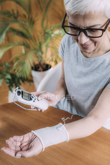 Femme âgée faisant une physiothérapie articulaire du poignet avec menottes d'électrode TENS conductrices (stimulation nerveuse électrique transcutanée). — Photo de stock