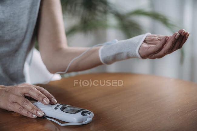 Senior woman doing wrist joint physical therapy with conductive TENS (transcutaneous electrical nerve stimulation) electrode cuff. — Stock Photo