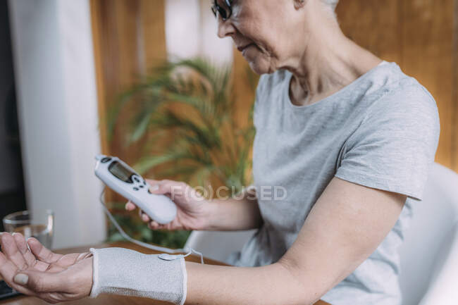 Femme âgée faisant une physiothérapie articulaire du poignet avec menottes d'électrode TENS conductrices (stimulation nerveuse électrique transcutanée). — Photo de stock