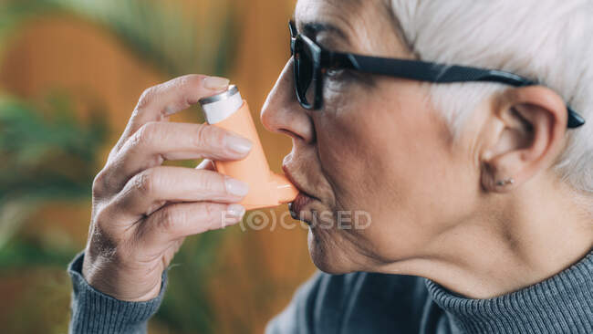 Femme âgée utilisant l'inhalateur d'asthme avec le tube d'extension. — Photo de stock