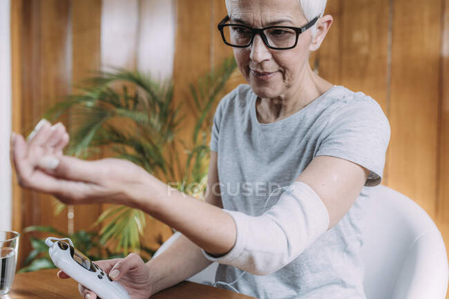 Старша жінка робить ліктьову фізичну терапію з TENS (перехресною електричною стимуляцією нервів) електродними брекетами . — стокове фото