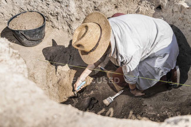 Archaeologist digging with hand trowel, recovering pottery from an archaeological site. — Stock Photo