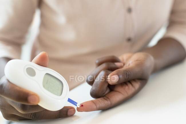 Mujer que usa un glucómetro para tomar una lectura de glucosa en sangre. - foto de stock