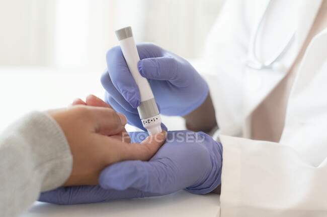 Médico usando una lanza para tomar una muestra de sangre del pinchazo del dedo de un paciente. - foto de stock