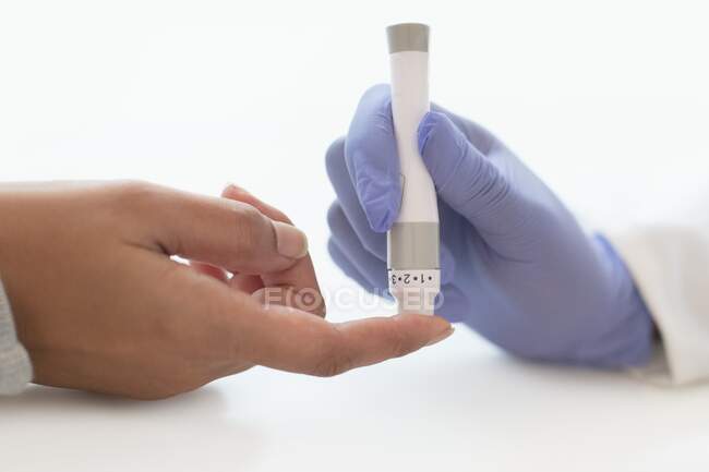 Doctor using a lance to take a finger prick blood sample from a patient. — Stock Photo