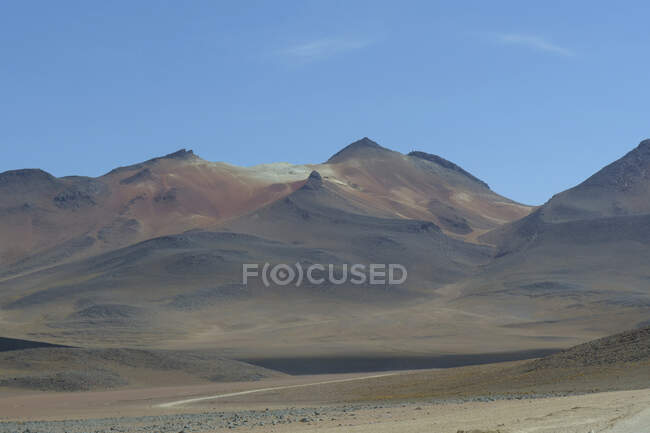 The high altitude Siloli Desert is surrounded by a string of mountains and extinct volcanoes. White volcanic deposits of borax, sodium tetraborate, and brown iron deposits give the landscape its unique colours. — Stock Photo