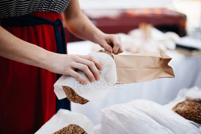 Woman putting loaf in paper bag — Stock Photo