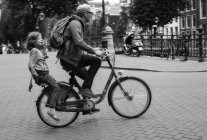 Amsterdam, Países Bajos - 18 de junio de 2016: el hombre y el niño en bicicleta en la calle de la ciudad - foto de stock