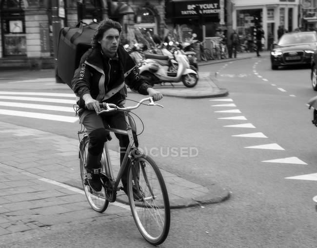 Amsterdam, Netherlands - June 18, 2016: man with large backpack ridding on bike at Amsterdam street — Stock Photo