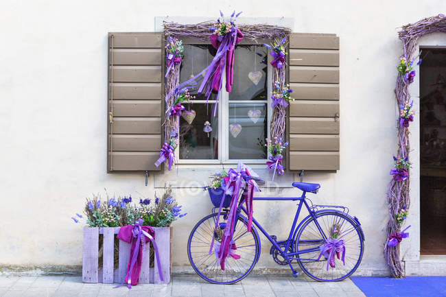 Bicicleta decorada de pie junto a la pared del edificio del pueblo de lavanda Venzone, Friuli Venezia Giulia, Italia - foto de stock