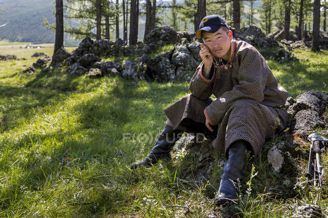 Mongolian man sitting on boulder in forest — Stock Photo