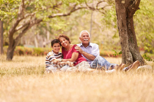 Abuelos Senior Pareja abrazando joven chico en hierba - foto de stock