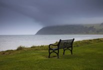 Bench on water edge with storm clouds — Stock Photo