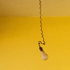 Lightbulb hanging on spiral cord against bright yellow background — Stock Photo