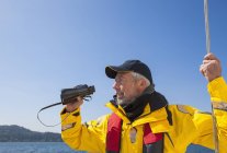 Un hombre mayor con prismáticos navegando cerca de la isla Vancouver; Columbia Británica, Canadá - foto de stock