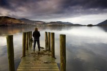 Una mujer de pie en un muelle de madera, Lago Derwent, Cumbria, Englan - foto de stock