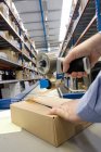 Cropped image of male hands packing box in warehouse beside large belt conveyor — Stock Photo