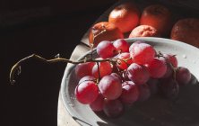 Uvas rojas en plato con mandarinas - foto de stock