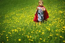 Junge spielt im Umhang wie ein Superheld im grünen Feld — Stockfoto