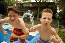Dos chicos jóvenes mostrando músculos contra la piscina en el patio trasero - foto de stock