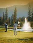 Two caucasian male golfers playing in course with fountain — Stock Photo