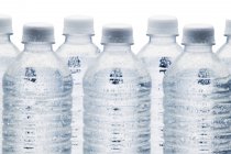 Linha de garrafas de água transparentes no fundo branco — Fotografia de Stock