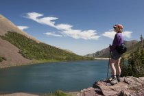 Senderista femenina con vistas a un lago mientras está de pie en un acantilado de roca ; - foto de stock