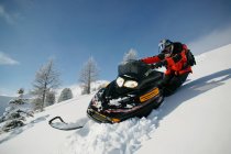Hombre conduciendo moto de nieve en la ladera cubierta de nieve - foto de stock