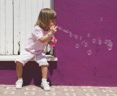 Vista da menina sentada na rua soprando bolhas — Fotografia de Stock