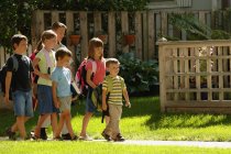 Escuela niños caminando sobre hierba verde - foto de stock